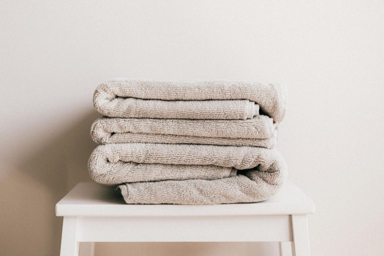 Pile de serviettes beige soigneusement pliées sur une étagère blanche épurée