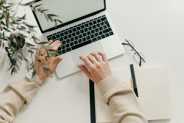 Bureau vue du dessus sur un ordinateur et des lunettes avec des mains sur le clavier